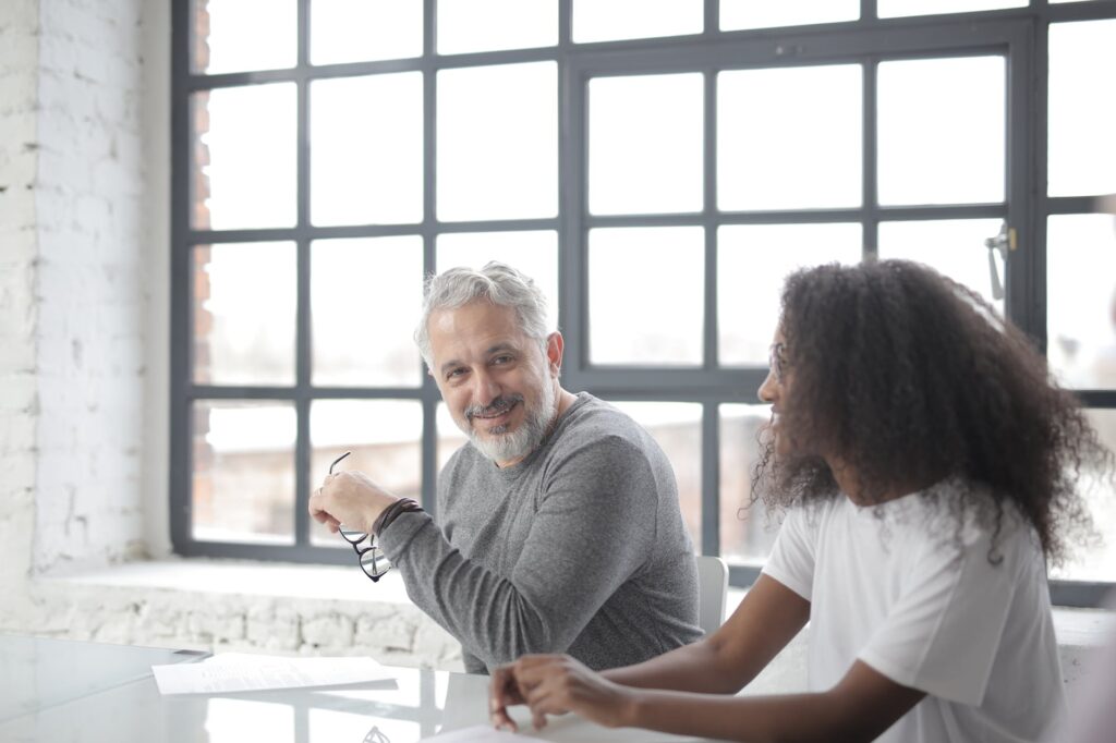 cheerful senior gray haired mentor supporting young black colleague in office business coach